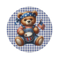 Round rug with a plush Americana teddy bear in denim overalls holding a toy drum and American flag on a blue and white gingham ground, shown flat