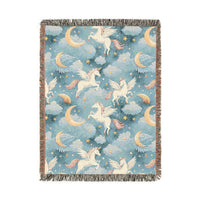 Woven blanket with cream winged unicorns, crescent moons, clouds and stars on a teal blue ground, shown flat