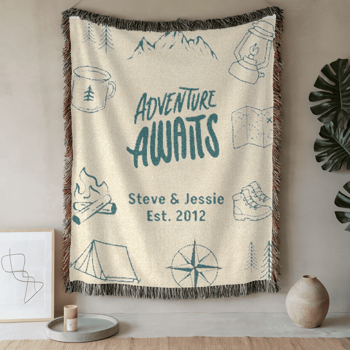 Adventure Awaits personalized woven blanket hung on a wall in a bright room with a plant
