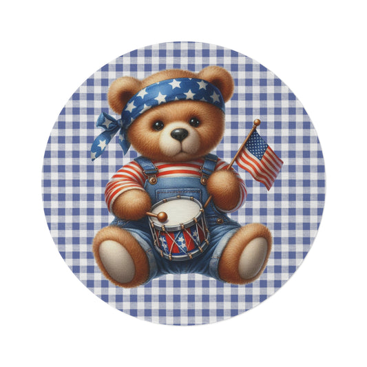 Round rug with a plush Americana teddy bear in denim overalls holding a toy drum and American flag on a blue and white gingham ground, shown flat