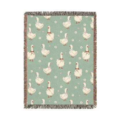 Sage green woven blanket with cream geese wearing rust, lilac and blue bows, with small daisies, shown flat