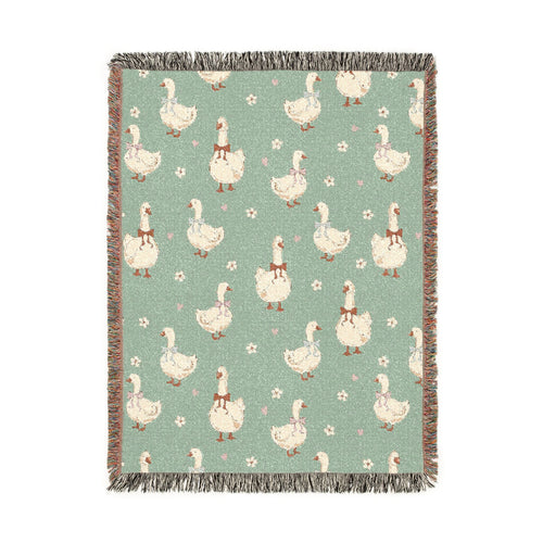 Sage green woven blanket with cream geese wearing rust, lilac and blue bows, with small daisies, shown flat
