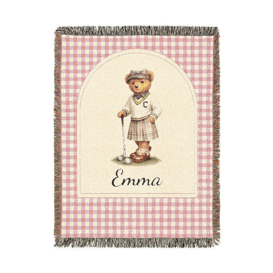 Personalized woven baby blanket with a golfing teddy bear and a name on a pink gingham border, shown flat
