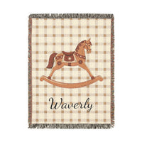 Personalized woven baby blanket with a rocking horse and a name on a beige gingham border, shown flat