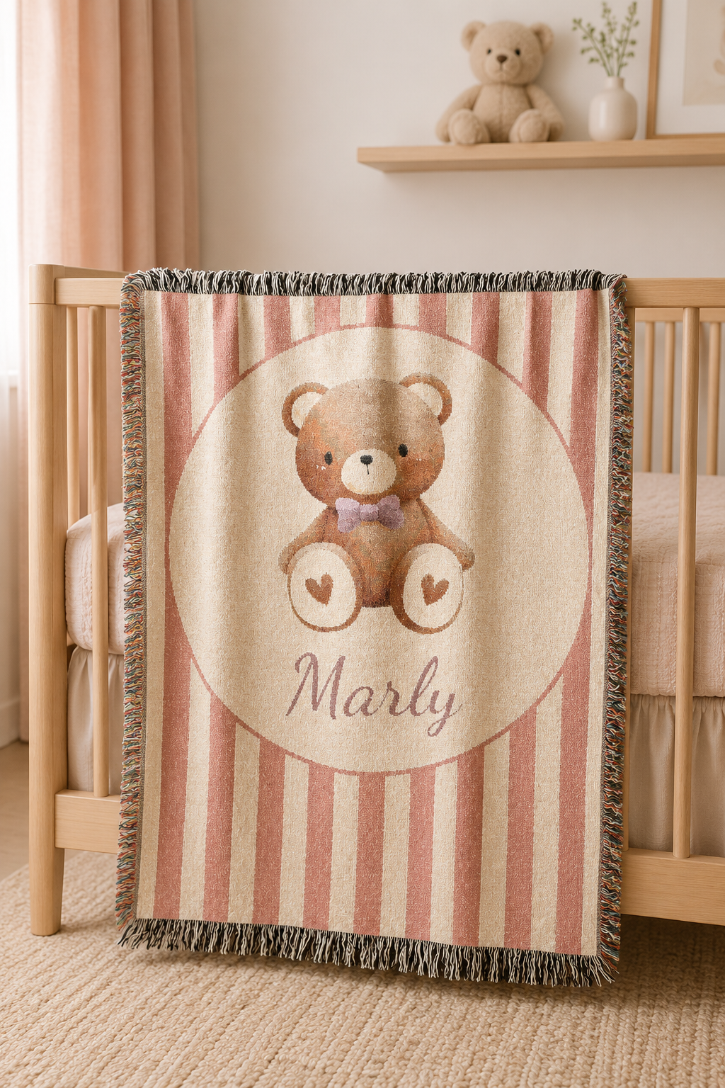 Personalized blush stripe teddy bear blanket draped over the rail of a crib in a warm nursery