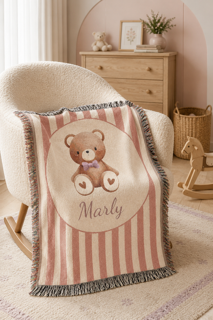 Personalized blush stripe teddy bear blanket draped beside a wooden dresser in a nursery