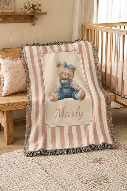 Personalized pink stripe teddy bear blanket over the rail of a crib in a bright nursery