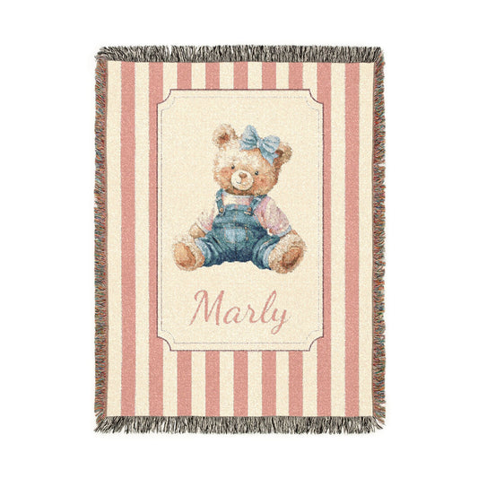 Personalized woven baby blanket with a watercolour teddy bear in dungarees and a blue bow on a pink and cream stripe, with a name woven in, shown flat