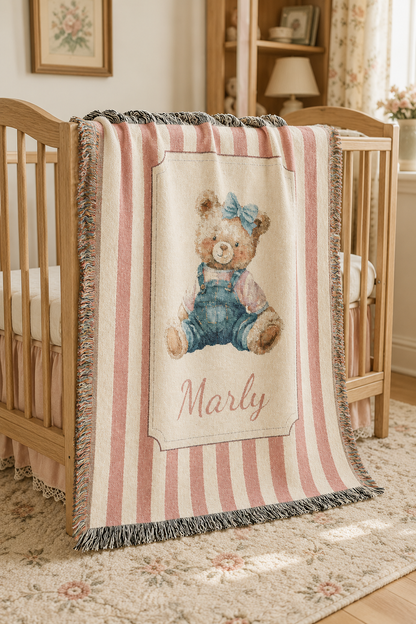 Personalized pink stripe teddy bear blanket over a chair by a window in a nursery