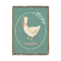 Personalized goose baby blanket with a cream goose in a pink ribbon inside a laurel circle on sage green, with a name woven in below, shown flat