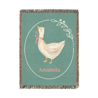 Personalized goose baby blanket with a cream goose in a pink ribbon inside a laurel circle on sage green, with a name woven in below, shown flat
