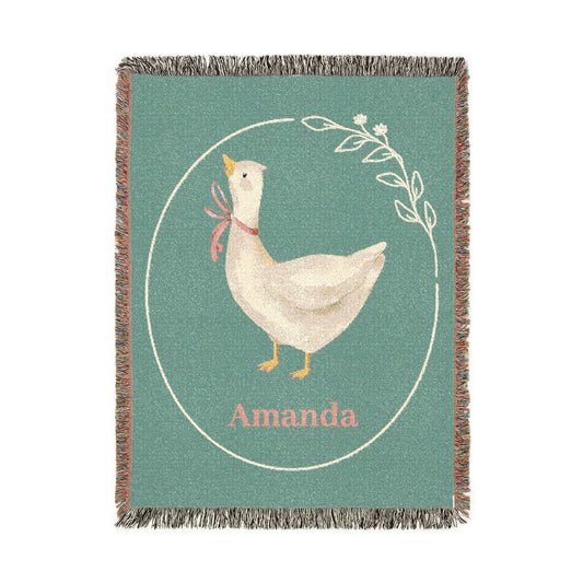 Personalized goose baby blanket with a cream goose in a pink ribbon inside a laurel circle on sage green, with a name woven in below, shown flat