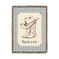 Personalized woven baby blanket with a cowboy hat and boots on a cream panel with a blue gingham border and a name woven in, shown flat