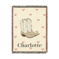Personalized woven baby blanket with cowgirl boots and soft pink hearts on cream, with a name woven in, shown flat