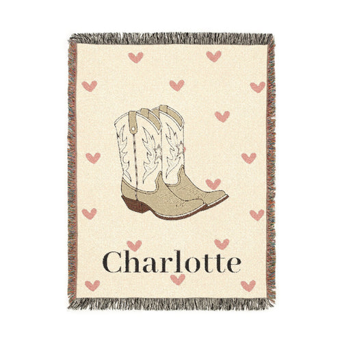 Personalized woven baby blanket with cowgirl boots and soft pink hearts on cream, with a name woven in, shown flat