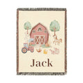 Personalized woven baby blanket with a red barn, tractor and farm animals on cream, with a name woven along the bottom, shown flat
