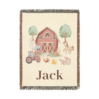 Personalized woven baby blanket with a red barn, tractor and farm animals on cream, with a name woven along the bottom, shown flat