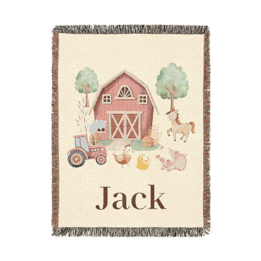 Personalized woven baby blanket with a red barn, tractor and farm animals on cream, with a name woven along the bottom, shown flat
