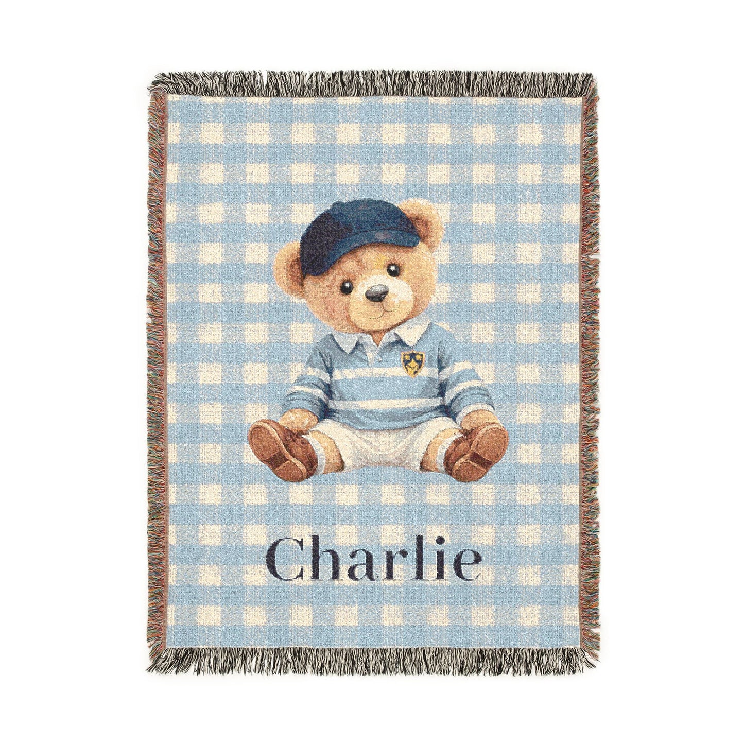Personalized woven baby blanket with a teddy bear in a blue cap and sweater on light blue gingham, with a name woven in, shown flat