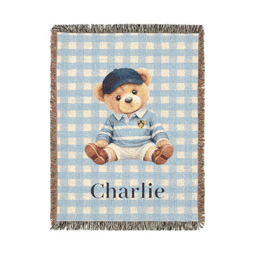 Personalized woven baby blanket with a teddy bear in a blue cap and sweater on light blue gingham, with a name woven in, shown flat