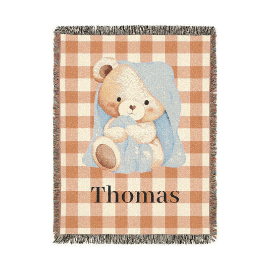 Personalized woven baby blanket with a cream teddy bear wrapped in a blue blanket on rust gingham, with a name woven in, shown flat