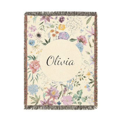 Personalized woven baby blanket with a wildflower meadow in lilac, blush and soft blue around a cream circle with a name woven in, shown flat