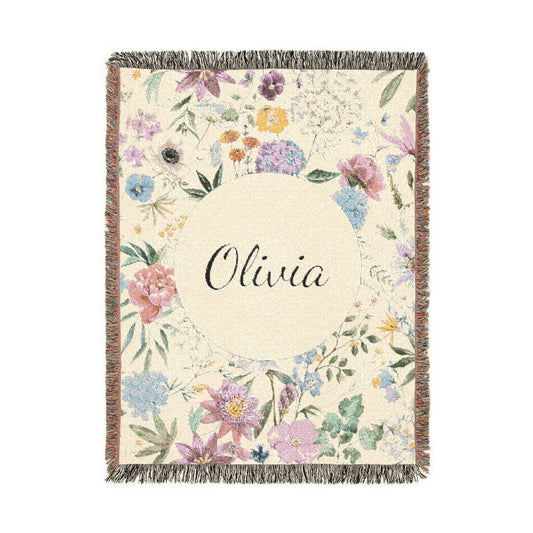 Personalized woven baby blanket with a wildflower meadow in lilac, blush and soft blue around a cream circle with a name woven in, shown flat