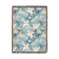 Woven blanket with cream winged unicorns, crescent moons, clouds and stars on a teal blue ground, shown flat
