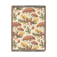 Woodland mushroom woven blanket featuring red-capped toadstools, golden oak leaves and acorns on a cream ground