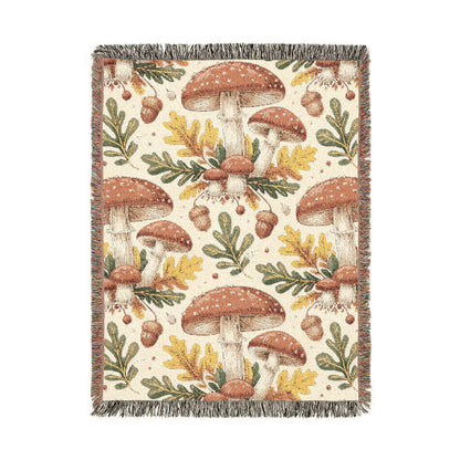 Woodland mushroom woven blanket featuring red-capped toadstools, golden oak leaves and acorns on a cream ground