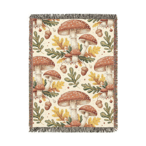Woodland mushroom woven blanket featuring red-capped toadstools, golden oak leaves and acorns on a cream ground